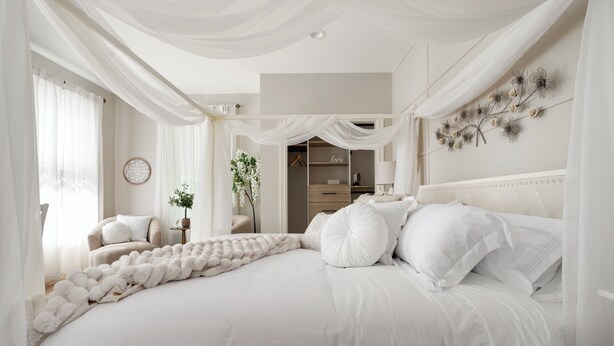 Une chambre à coucher avec un grand lit, une table de chevet, une chaise, une armoire et un élément décoratif mural.