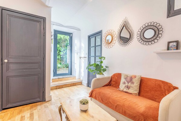 A room with a wooden floor, a sofa with an orange blanket, a potted plant, and decorative wall mirrors. - Charming 1bdr/2p Flat With a Garden (Marseille)