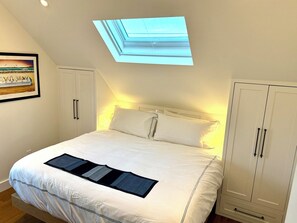A bedroom with a skylight, a bed with white bedding, a framed picture on the wall, and white wardrobes. - Modern West End Retreat with 2 King Beds (Provincetown)