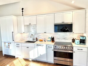 A modern kitchen with white cabinets, a stainless steel stove, and a microwave. - Modern West End Retreat with 2 King Beds (Provincetown)