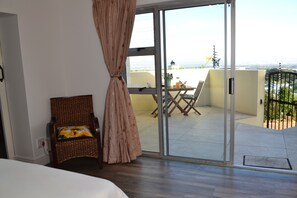 Ein Zimmer mit einem Bett, ein Korbstuhl mit Kissen, eine Schiebetür zu einem Außenbereich mit Tisch und Stühlen.