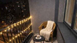 Ein Balkon mit einem Korbstuhl, einem Tisch mit einer Tasse und Lichterketten.
