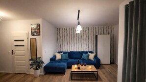 Ein Wohnzimmer mit einem blauen Sofa, einem Couchtisch mit Kerzen, einer Pendelleuchte und einer Pflanze.