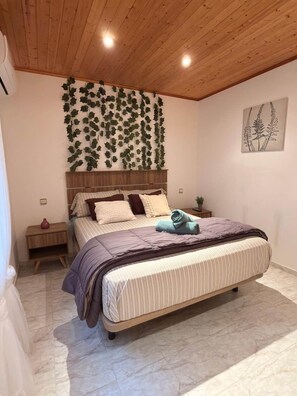 Ein Schlafzimmer mit Holzbalkendecke, einem Bett mit gestreifter Bettwäsche, einer Wandpflanze, einem Nachttisch mit Vase und einer gerahmten Pflanzenillustration.