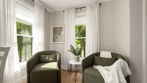 Una habitación con dos sillones verdes, una pequeña mesa blanca con una planta y un cuadro en la pared.
