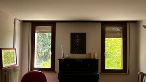 A room with a piano, a red chair, a wooden floor, and two windows with blinds. - Historic Palazzo with Pool & Castle View (Sanguinetto)