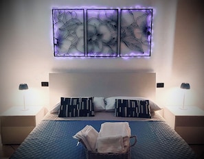 Una camera da letto con un letto, due comodini, un punto luce a parete e un pannello decorativo sopra il letto.