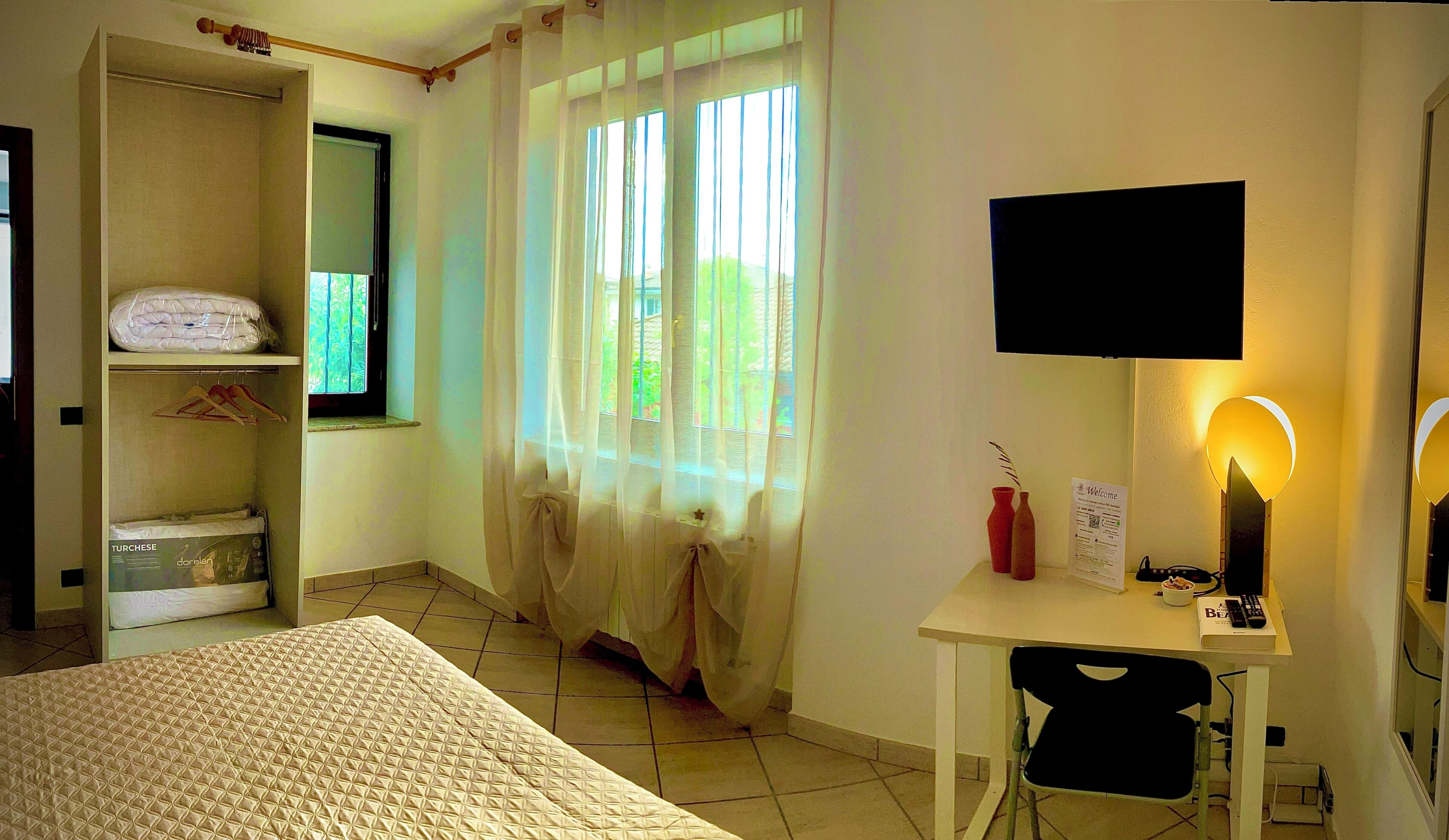 Une chambre à coucher avec un lit, un bureau avec une chaise, une télévision et une fenêtre avec des rideaux.