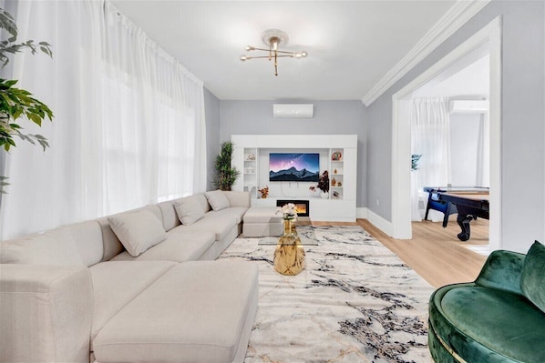 A living room with a beige sofa, a green armchair, a coffee table, and a TV on a white wall.
