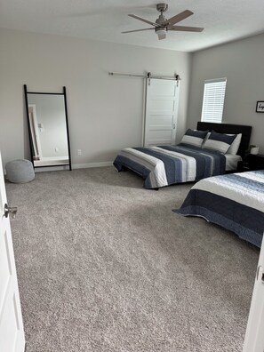 A bedroom with two beds, a ceiling fan, a door, and a window with blinds.
