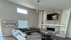 A modern living room with a sectional sofa, a dining table with chairs, a fireplace, and a mounted TV.
