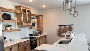 A modern kitchen with wooden cabinets, a marble countertop, a built-in oven, and a central island with bar stools.