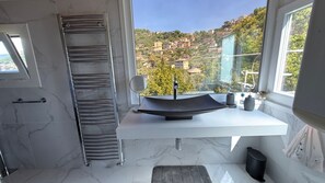 Ein modernes Badezimmer mit einem gewölbten Waschbecken, einem Handtuchhalter und Blick auf eine Hügelstadt.