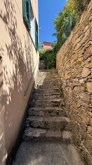 Eine schmale Steintreppe führt zu einem Gebäude mit einer beige gefärbten Wand und grünen Fensterläden.