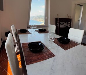 Ein Esstisch mit vier schwarzen Schüsseln, zwei Weingläsern und Meerblick durch ein Fenster.