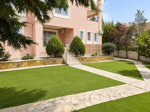 A pink building with a stone staircase leading to a door, surrounded by well-maintained lawns and stone pathways. - Treasure B B - Garden Stay in Paloukia Salamina (Salamis)
