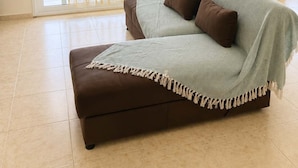 A room with a brown sofa, a light-colored throw blanket, and a view through a window with sheer curtains. - Treasure B B - Garden Stay in Paloukia Salamina (Salamis)