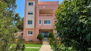 A multi-story building with a pink facade, a stone pathway leading to the entrance, and green landscaping. - Treasure B B - Garden Stay in Paloukia Salamina (Salamis)