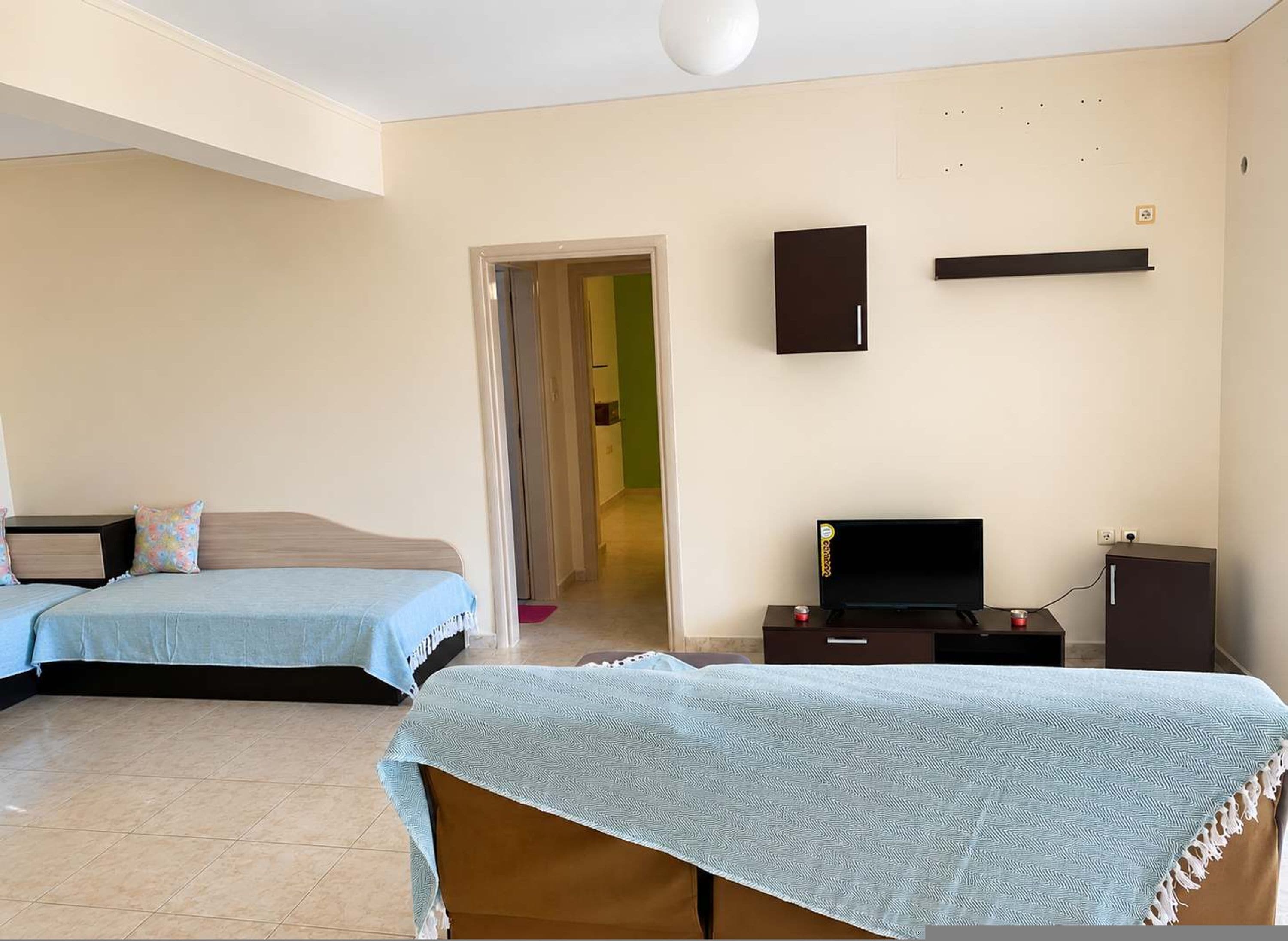 Ein Hotelzimmer mit zwei Betten, einem Fernseher, einem kleinen Schrank und einer Tür zu einem anderen Raum.