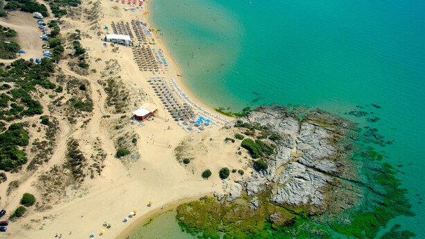 An aerial view of a beach with rows of beach umbrellas, a few people, and a rocky outcrop in the water. - Studio Aspilon Pool and Mountain Views Near Drama (Drama)