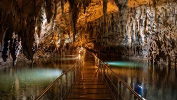 Una cueva con pasarela de madera y barandillas de metal, rodeada de estalactitas y estalagmitas.