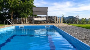 A rectangular swimming pool with clear blue water, surrounded by a stone wall, a metal fence, and a covered seating area. - Studio Aspilon Pool and Mountain Views Near Drama (Drama)