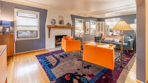 Una sala de estar con chimenea, sillones anaranjados, un sofá azul y una alfombra estampada.