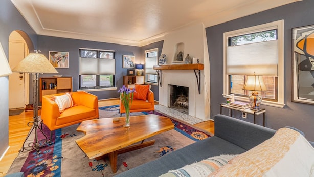Una sala de estar con chimenea, sofás naranja, una mesa de centro de madera y un sofá azul.