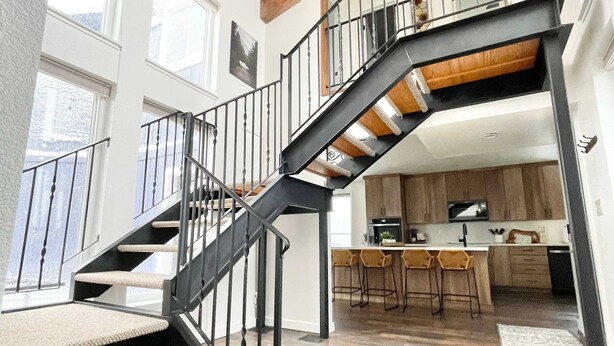 A modern interior with a wooden ceiling, a staircase with black railings, and a kitchen area. - Reno Retreat - 3BR Oasis w Swim Spa Hot Tub (Reno)