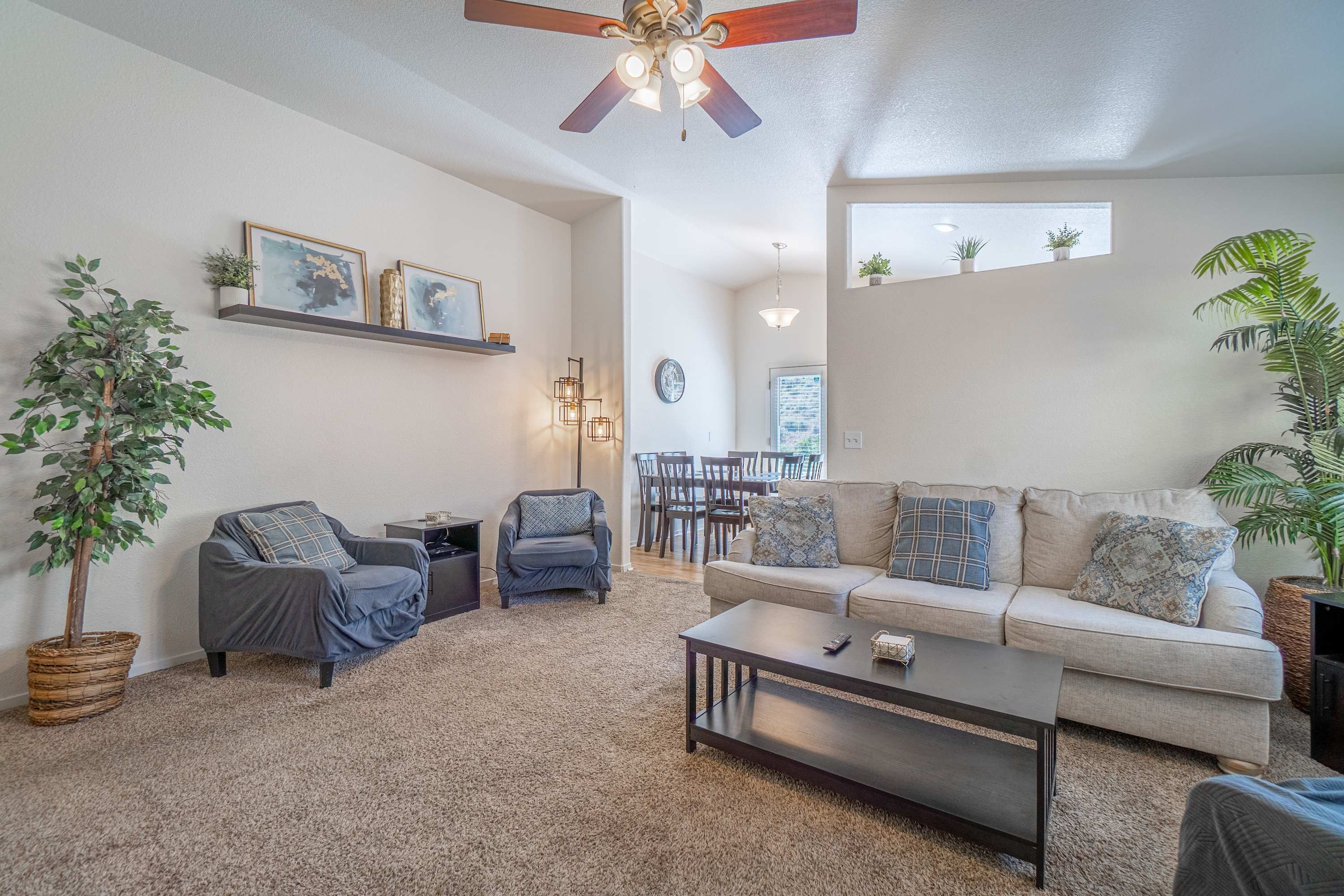 A living room with a sofa, chairs, a coffee table, a ceiling fan, and a dining area in the background.