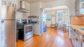 A modern kitchen with stainless steel appliances, a wooden floor, and a view into the dining area. - Midtown Sanctuary w Pac-man (Reno)