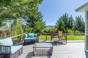 Eine Terrasse mit Korbmöbeln, einem Glastisch und Blick auf Bäume und Berge.