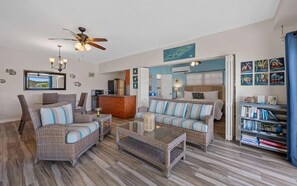 A living room with wicker furniture, a ceiling fan, a bookshelf, and a view of the outside.