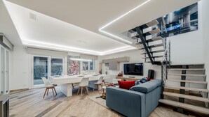 A modern living room with a sofa, dining area, and staircase. - Villa Padana (Piumazzo)