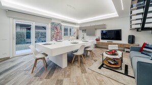 A modern living room with a large dining table, a flat-screen TV, and a staircase. - Villa Padana (Piumazzo)