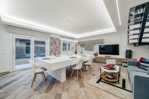 A modern living room with a large dining table, a flat-screen TV, and a staircase. - Villa Padana (Piumazzo)