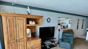 Ein Wohnzimmer mit einem Holzkabinett, einem Fernseher, einem blauen Sessel und einer Lampe.