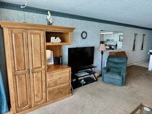 Ein Wohnzimmer mit einem Holzkabinett, einem Fernseher, einem blauen Sessel und einer Lampe.