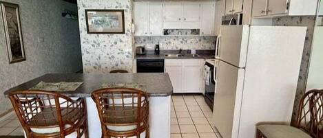 A compact kitchen with a central island, two wooden chairs, a refrigerator, and a microwave.