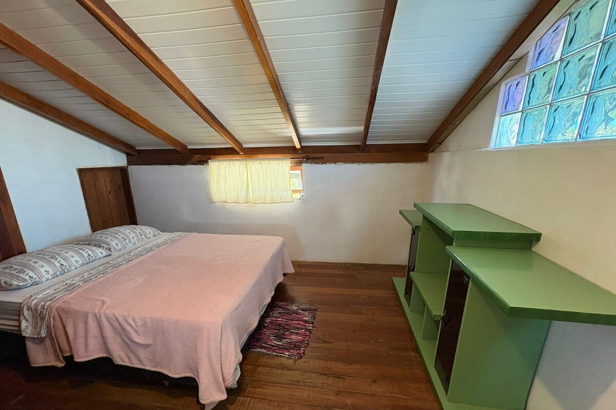 Un dormitorio con cama, un ventanal con cortinas, un banco verde y vigas de madera en el techo.