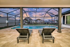 Ein überdachter Außenbereich mit Pool, zwei Liegestühlen und Blick auf Häuser im Hintergrund.