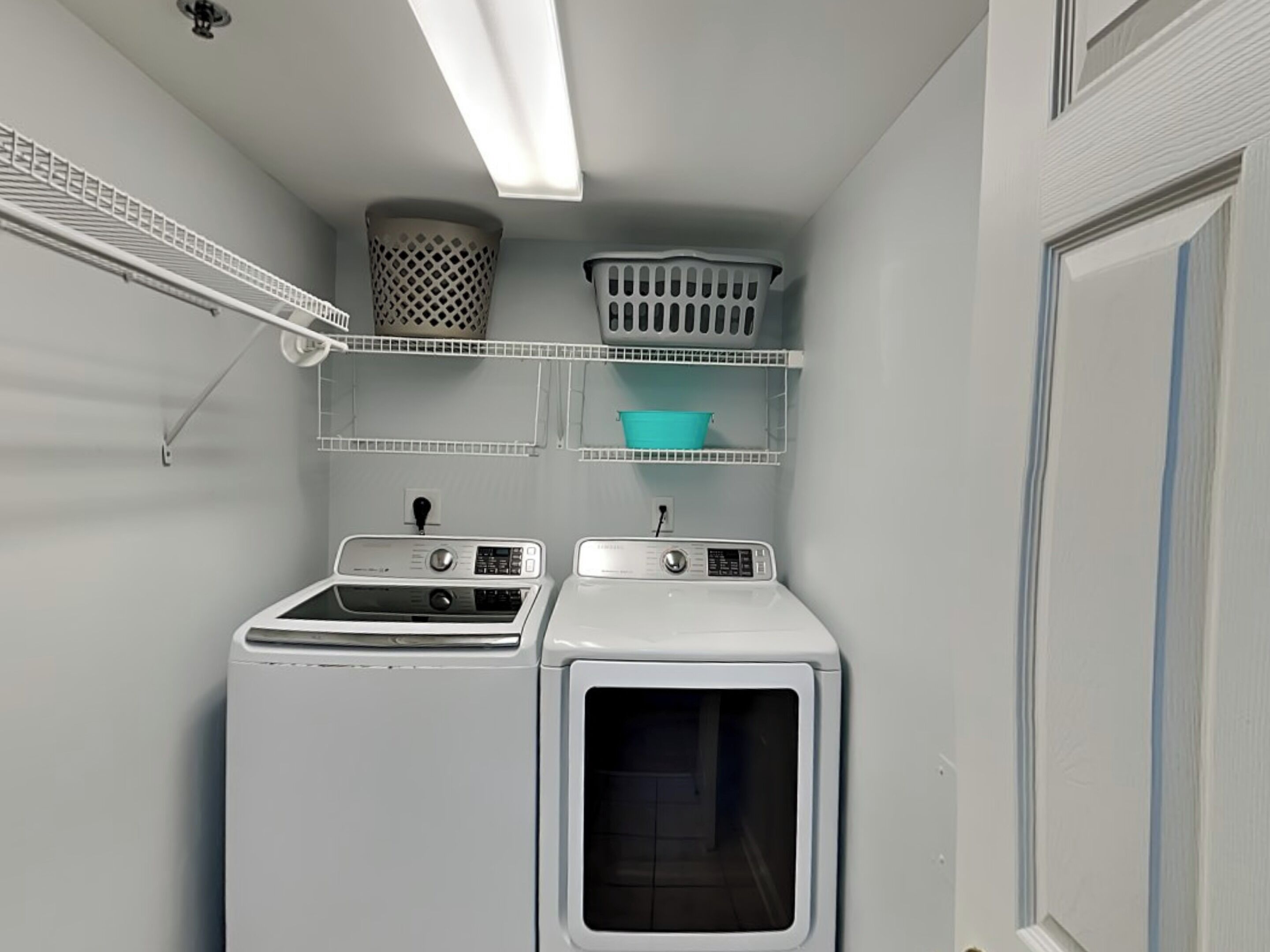 A laundry room with two washing machines, a drying rack, and shelves with baskets.