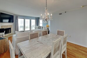 Ein modernes Wohnzimmer mit einem weißen Esstisch, Korbstühlen, einer Chandelüster, einem Flachbildfernseher und einem Kamin.