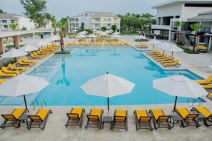 Una piscina con lettini e ombrelloni, circondata da un edificio con diversi piani e balconi.