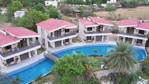 Un resort con piscina central, varias construcciones de dos pisos con balcones y exuberante vegetación circundante.