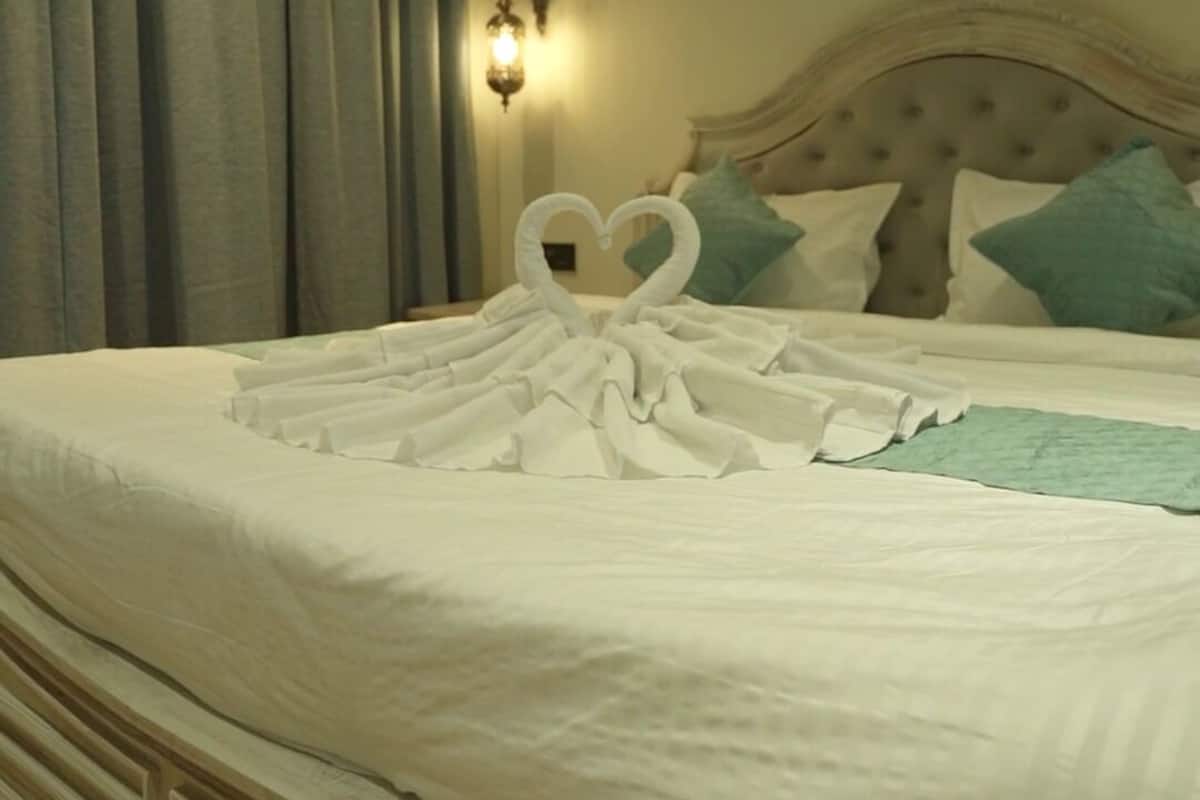 Habitación de hotel con cama, cortinas, apliques de pared y una decoración de toallas en forma de corazón.