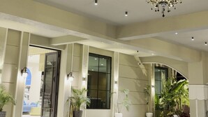 Un vestíbulo amplio con techo alto, iluminación empotrada, un candelabro y plantas en macetas.