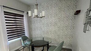 A dining area with a round table, four chairs, a chandelier, and a brick wall. - Comfortable Private Room – Central Winnipeg (Winnipeg)