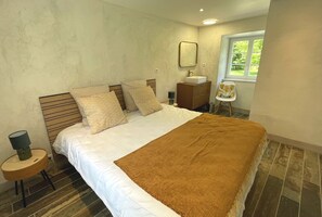 Ein Schlafzimmer mit Bett, Nachttisch, Lampe, Kommode, Spiegel und Fenster.
