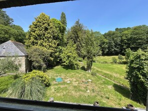 Ein Ausblick auf eine begrünte Wiese mit Bäumen und einem Steinhaus.